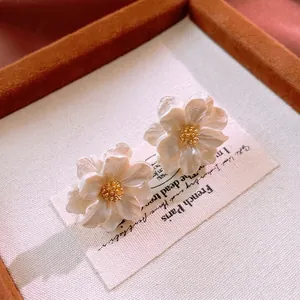 Elegant white floral earrings with golden core on textured cardstock and wooden frame