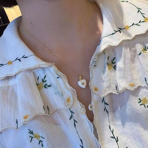 Close-up of white heart enamel pendant necklace on model with dainty golden chain link