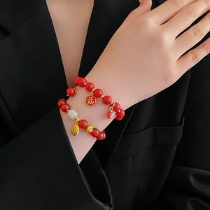 Gros plan d'un bracelet à double couche de perles rouges avec breloque Fu dorée et jade