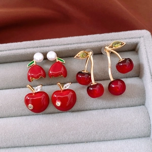 Detailed macro shot of red cherry, apple, and bell earrings on a velvet jewelry tray
