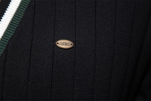 Macro dettaglio della maglia a costine nera e dell'emblema in ottone sul cardigan