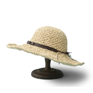Detail of cream straw hat with brown leather band and metal buckle on wooden stand