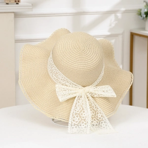 Detail of beige straw hat with large wavy brim and elegant white lace floral bow