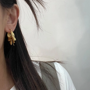Close-up of a 18K gold plated leaf-shaped brass hoop earring on model ear