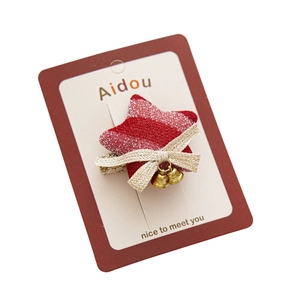 Red and white striped star hair clip with golden bow and bell on display card