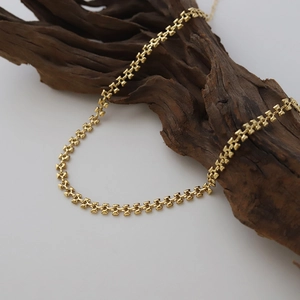 Close-up of golden geometric linked necklace displayed on textured wood base