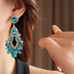 Close-up of elegant gold drop earrings with blue gemstones and rhinestones on a model