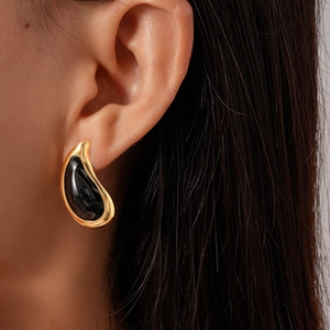 Close-up of elegant gold teardrop earrings with black enamel inlay on a model