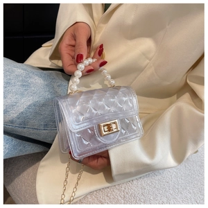 Detail of mini transparent quilted bag with large pearl handle and golden chain strap