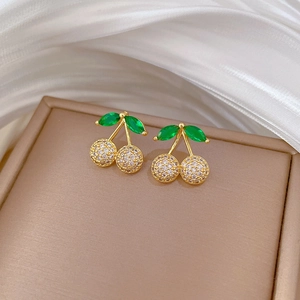 Elegant gold cherry stud earrings with green leaf and sparkling crystals on silk