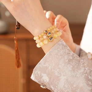 Detail of yellow citrine bead bracelet set with gold floral charms worn on a wrist