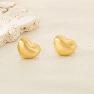 Détail de boucles d'oreilles cœur dorées avec finition mate brossée sur fond texturé