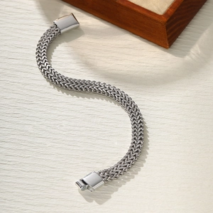 Detailed view of silver stainless steel woven bracelet with magnetic clasp on beige surface