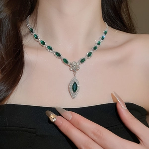 Close-up of a luxury silver necklace featuring green gemstones and sparkling rhinestones