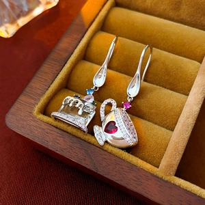 Detail view of asymmetric silver earrings shaped as a cake and coffee cup with colored gems