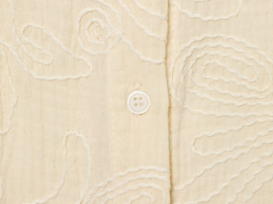 Gros plan détaillé du tissu en lin beige avec broderie ondulée et boutons blancs
