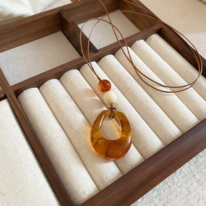 Close-up of amber resin pendant on brown leather cord inside a wooden jewelry box