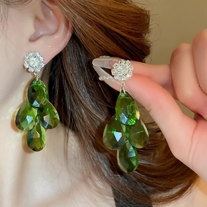 Macro view of emerald green teardrop multi-layer clip earrings with crystal cluster