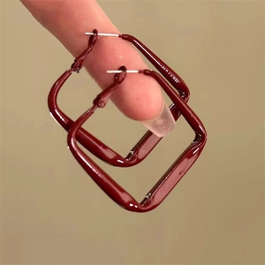 Detail shot of deep red square hoop earrings with polished finish held on fingers