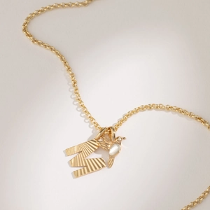 Close-up of golden O-chain necklace featuring a textured letter M and bird charm