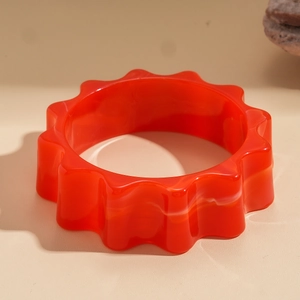 Dettaglio macro del bracciale in acrilico rosso con motivo a onde su sfondo beige caldo