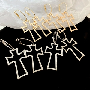 Macro detail of large hollow cross earrings with engraved metallic textures in gold and silver