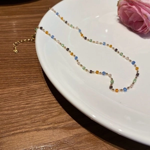 Colorful square crystal bead necklace with gold accents presented on a white plate