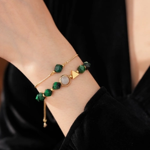 Detail of layered gold bracelet featuring green geometric beads and a triangle charm