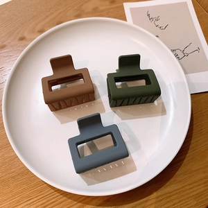 Three matte square hollow hair claws in brown, green, and blue on a white ceramic plate