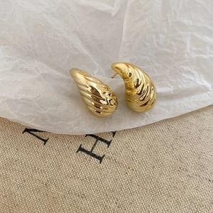 Detailed close-up of golden teardrop earrings with elegant spiral texture and polished finish