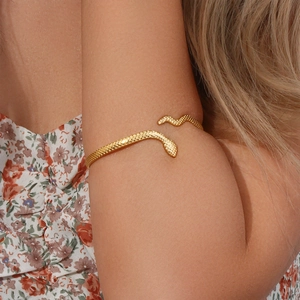 Close-up of golden snake-shaped open arm cuff on model's arm with floral background