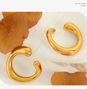 Detail of C-shaped gold ear cuffs with a polished mirror finish on white textured fabric