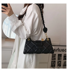 Model wearing black quilted shoulder bag with unique woven strap in a chic interior setting