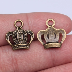 Macro shot of small bronze crown pendants on fingertips showing front and back details