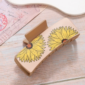Matte light brown rectangular hair claw clip with yellow sunflower patterns on wood