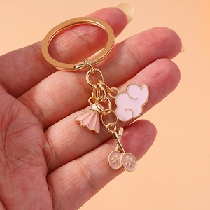 Pink badminton and tennis racket charms on a golden keychain held against a soft background