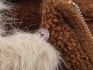 Dettaglio pelliccia marrone con pompon di peluche bianco e cerniera color argento