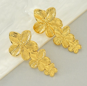 Macro detail of gold-plated triple flower earrings with brushed metallic texture