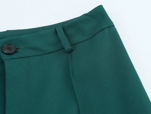 Close-up of waistline detail on dark green trousers featuring button and belt loops