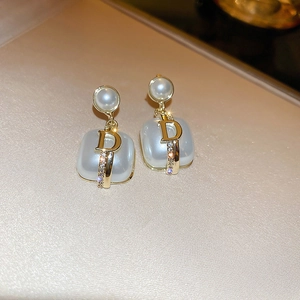 Macro shot of pearl flower drop earrings with a golden D initial and crystal accents