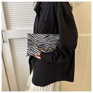 Close-up of zebra pattern envelope clutch bag with gold metal trim held by a model
