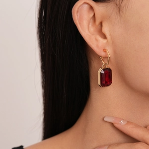 Detailed close-up of dark red rectangular gemstone earring with a golden geometric buckle