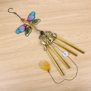 Macro detail of metal dragonfly wind chime with colorful wings on light wood background