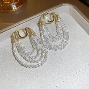 Vue macro détaillée de boucles d'oreilles dorées en U avec pampilles de perles multicouches