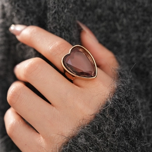 Detail of a large gold cocktail ring featuring a heart-shaped brown gemstone on finger