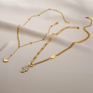 18K gold plated Hamsa Hand and heart charm layered necklace on soft grey fabric background