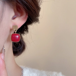Close-up of red enamel square drop earrings with vintage gold brushed metal texture
