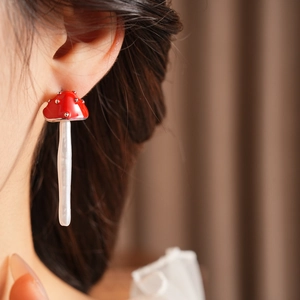 Close-up of a model wearing red mushroom earrings with white spots and a glossy finish