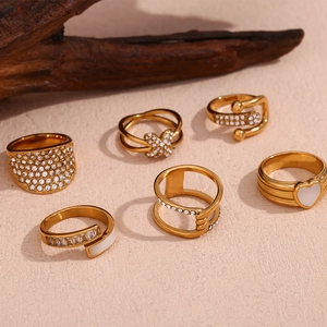 Set of 6 gold rings with cubic zirconia and heart charms displayed on a textured background
