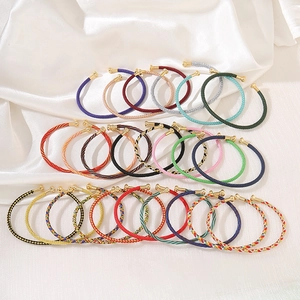 Close-up of colorful woven rope open bracelets with golden metal caps on silk background